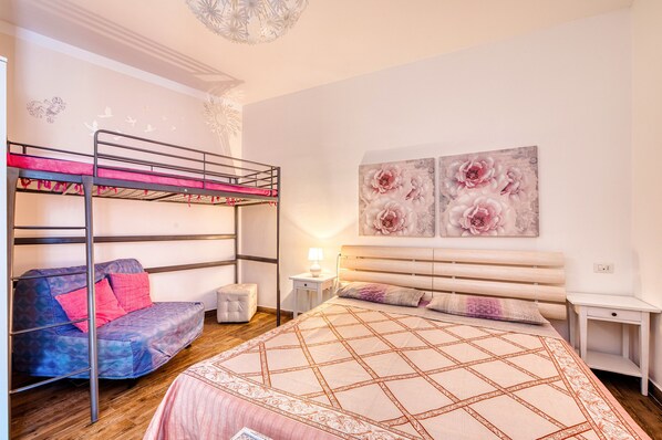 A bedroom with bunk beds, a bed with a patterned bedspread, a nightstand, a lamp, and floral artwork on the wall. - Vrbo Property (Foligno)