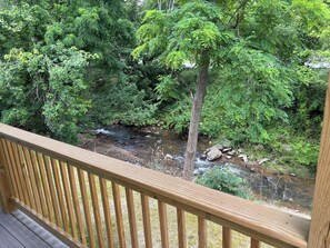 Une terrasse en bois donnant sur une zone boisée, avec un ruisseau.