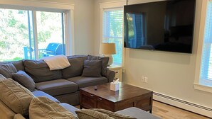 A modern living room with a sectional sofa, a flat-screen TV, and large windows.