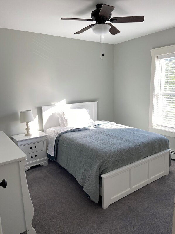 Un dormitorio con cama, mesita de noche, lámpara y ventilador de techo.