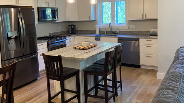 A modern kitchen with white cabinets, a stainless steel refrigerator, a microwave, and a large island with chairs.