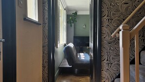 A narrow hallway with a wooden floor leading to a room with a bed and a desk. - The Lodge Stanwell (Staines)