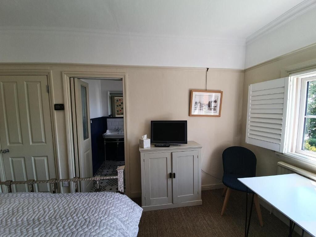 Ett hotellrum med en säng, ett skrivbord, en tv-apparat på ett skåp, en stol och ett fönster med persienner.