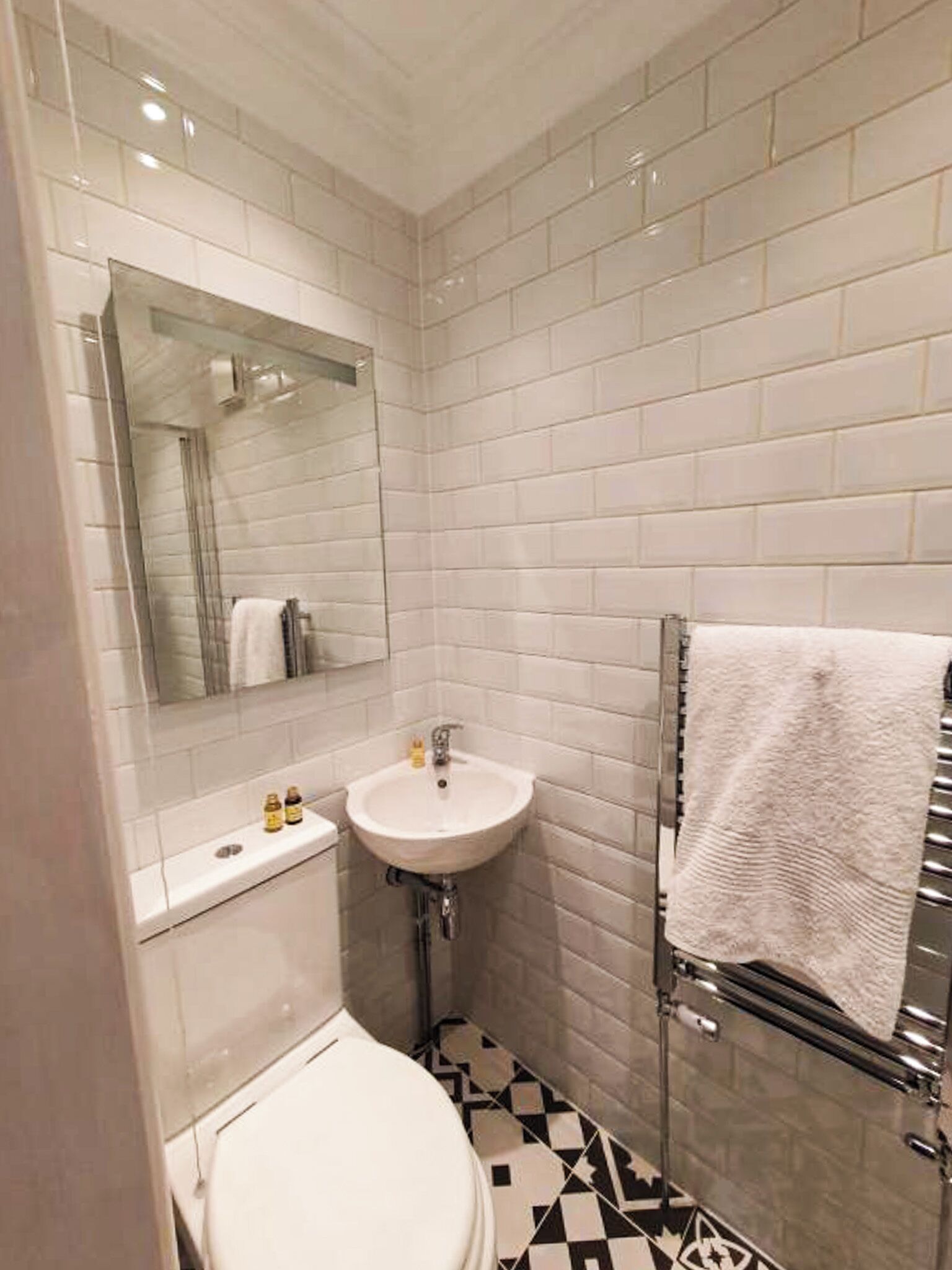 Une salle de bain avec des carreaux de céramique blancs rectangulaires, un lavabo blanc, un miroir et un porte-serviettes.