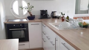 Moderni keittiö, jossa on valkoiset kaapit, musta uuni, kahvinkeitin ja pesuallas.