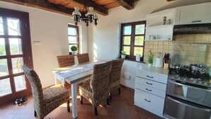 A kitchen with a dining table, wicker chairs, a chandelier, white cabinets, and a stove. - Villa a Balaton-Felvidéken, ahol jakuzziban gyönyörködhet a tó panorámájában (Vászoly)