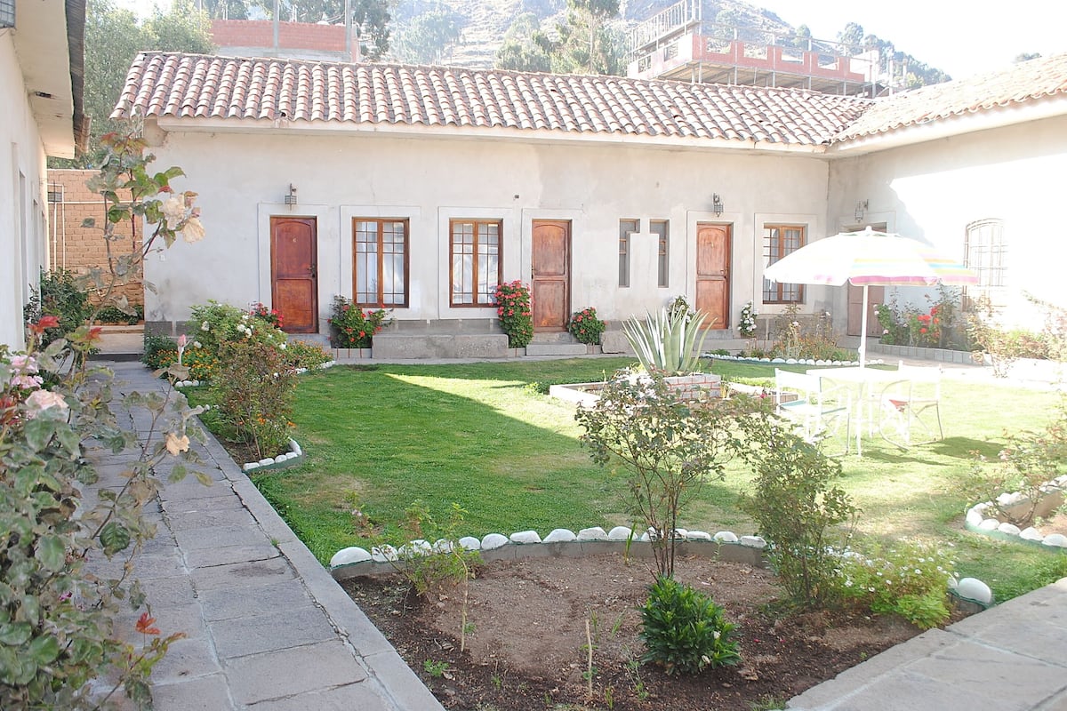A courtyard with a white building, a lawn, and a garden with various plants and flowers.
