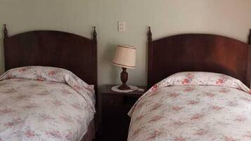 Una habitación con dos camas de madera con ropa de cama floral, una mesita de noche pequeña con una lámpara y un cuadro en la pared.