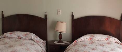 Una habitación con dos camas de madera con ropa de cama floral, una mesita de noche pequeña con una lámpara y un cuadro en la pared.