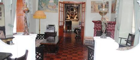 Una habitación con suelo de parquet de madera, una chimenea, una araña y un cuadro en la pared.