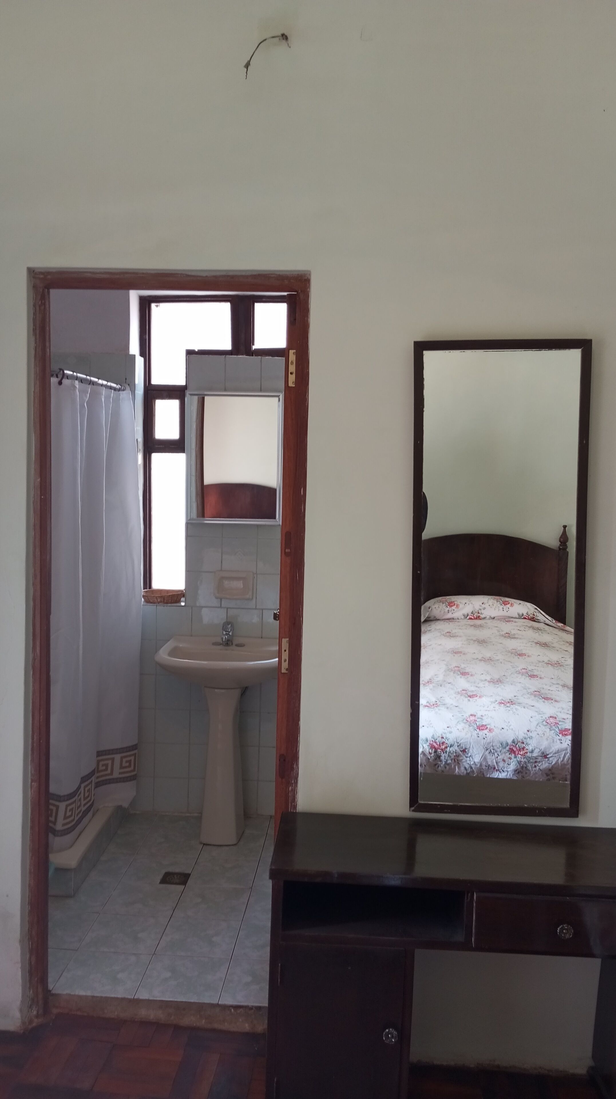 Ein Zimmer mit einem Bett, einem Nachttisch, einem Spiegel, einem Waschbecken und einer Dusche.