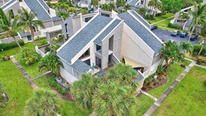 A modern residential building with a sloped roof, multiple balconies, and a well-maintained lawn with palm trees. - Beachside townhouse with private office space (Jupiter)