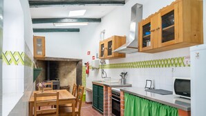 A compact kitchen with a brick oven, wooden cabinets, and a dining area with a table and chairs. - CAM - Aguarelas de Lisboa T1 (Obidos)