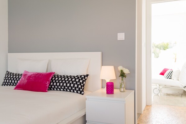A neatly arranged bedroom with a bed, bedside table, lamp, and a vase with flowers.