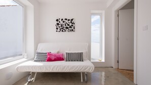 A white sofa with patterned cushions, a wall art piece, and a view through a window. - ST Apart 01 in Atouguia da Baleia (Peniche)