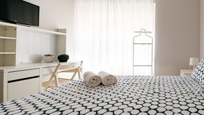 A bedroom with a bed, a desk, a chair, a TV, a window with curtains, and a hanging rack. - Mar Alta - Estelas (Peniche)