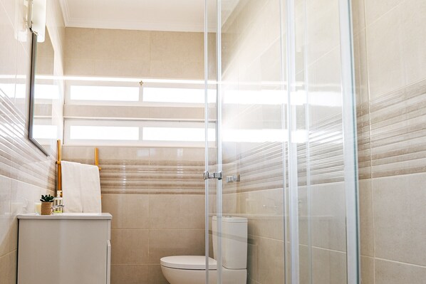 A modern bathroom with a glass shower enclosure, a toilet, and a sink with a towel hanging on the wall.