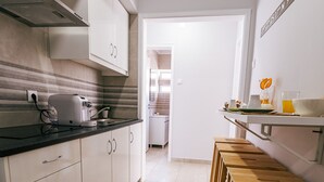 A narrow kitchen with white cabinets, a black countertop, and a small dining area with a white table and benches. - Mar Alta - Baleal in Peniche (Peniche)
