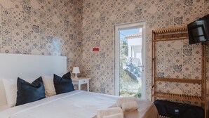 A bedroom with a bed, pillows, a bedside table with a lamp, a TV, and a window with a view. - Encosta d Bidos T1 (Obidos)