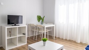 A modern living room with a flat-screen TV, a dining table with chairs, a coffee table with a plant, and sheer white curtains. - Mar Alta - Gamb a (Peniche)