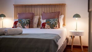 Ein ordentlich bezogenes Bett mit einem Holz-Kopfteil, zwei Nachttischen mit Lampen und einer Auswahl gemusterter Kissen.