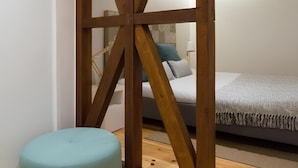 Ein Zimmer mit einer Holzwand, einem petrolfarbenen Ottomanen und einem Bett mit gemustertem Überwurf.