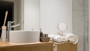 Ein modernes Badezimmer mit einem großen, weißen Waschbecken, einem hölzernen Waschtisch, einer Duschkabine aus Glas und einem Schachbrettmuster auf dem Boden.