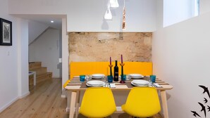 A dining area with a wooden table set for two, yellow chairs, and a brick accent wall.