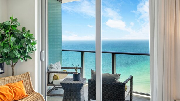 A balcony with wicker furniture, a potted plant, and a view of the ocean.