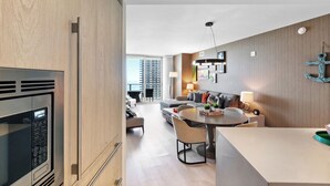 A modern kitchen with a built-in microwave, a dining area with a round table and chairs, and a living area with a sofa and a lamp.