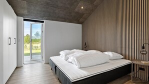 A modern bedroom with a large bed, a wooden slatted wall, and a view through a glass door. - Stunning home in Sæby with sauna (Sæby)