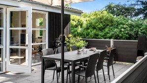 An outdoor patio with a table and chairs, a grill, and a view of a garden.