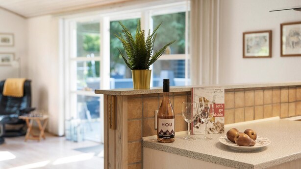 A kitchen counter with a bottle of wine, a potted plant, and a plate of bread.