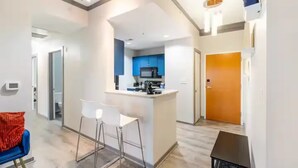 A modern interior with a kitchen area, a dining space with bar stools, and a hallway leading to a door. - Downtown Dream: 2-Bed Condo with Pool & Parking! (Charlotte)