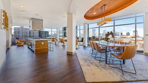 A spacious, modern kitchen with a large island, a dining area with a long table and chairs, and large windows offering a city view.