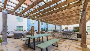 An outdoor patio area with wooden pergola, stone-tiled flooring, and a barbecue station.