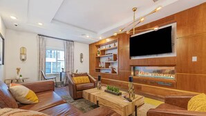 A modern living room with leather sofas, a wooden coffee table, and a large flat-screen TV mounted on a wooden wall.