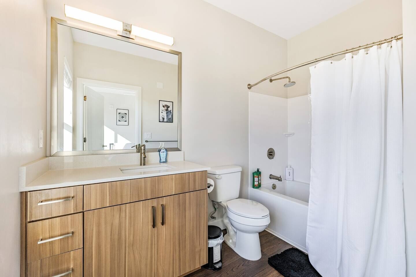 Un baño moderno con tocador de madera, inodoro, ducha con cortina y un espejo grande.