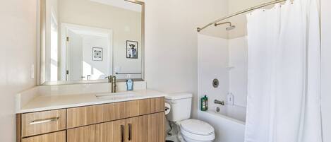 Un baño moderno con tocador de madera, inodoro, ducha con cortina y un espejo grande.