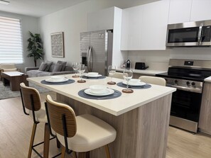 Una cocina moderna con una isla central, electrodomésticos de acero inoxidable y un comedor con sillas y una mesa para dos.