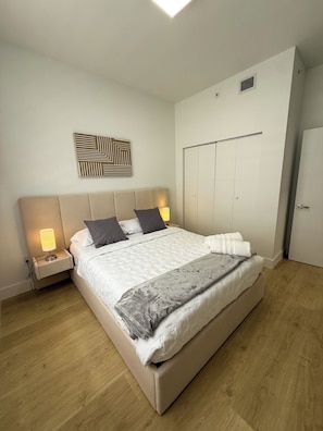Un dormitorio con cama, lámparas de noche, armario y una obra de arte colgada en la pared.