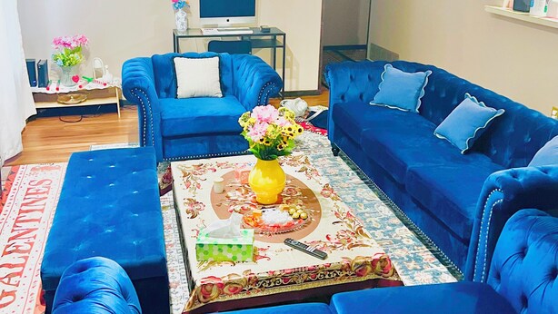 Una sala de estar con sofás azules, una mesa de centro con un jarrón, un reloj en la pared y una computadora en un escritorio.