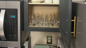 Una cocina equipada con microondas, cafetera y una alacena con cristalería y tazas.