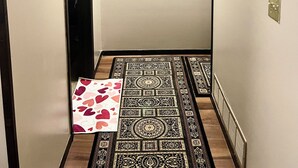 Un pasillo con alfombra estampada, una puerta, un termostato y un cuadro con una cascada.