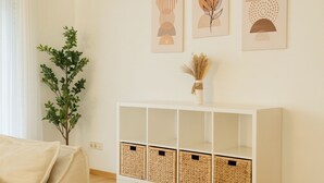 Una sala de estar con un sofá blanco, una consola blanca con cestas tejidas, y tres obras de arte enmarcadas en la pared.