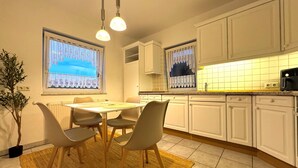 Una cocina moderna con armarios blancos, una mesa de comedor con sillas e iluminación colgante.