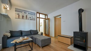 A modern living room with a grey sofa, a small table with a book, a grey pouf, a wooden coffee table, a black wood-burning stove, and a painting of birds on a post. - Pet friendly home in Bjelovar with sauna (Curlovac)