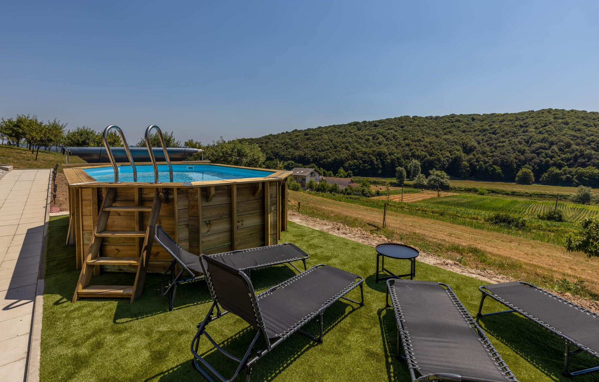 An outdoor swimming pool with wooden deck, lounge chairs, and a scenic view of a forested hill.