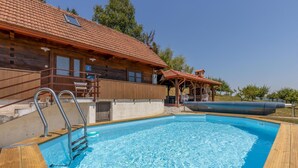 A swimming pool with a wooden deck, a wooden house with a red-tiled roof, and a covered outdoor seating area. - Awesome home in Jaskovo with heated swimming pool (Jaskovo)