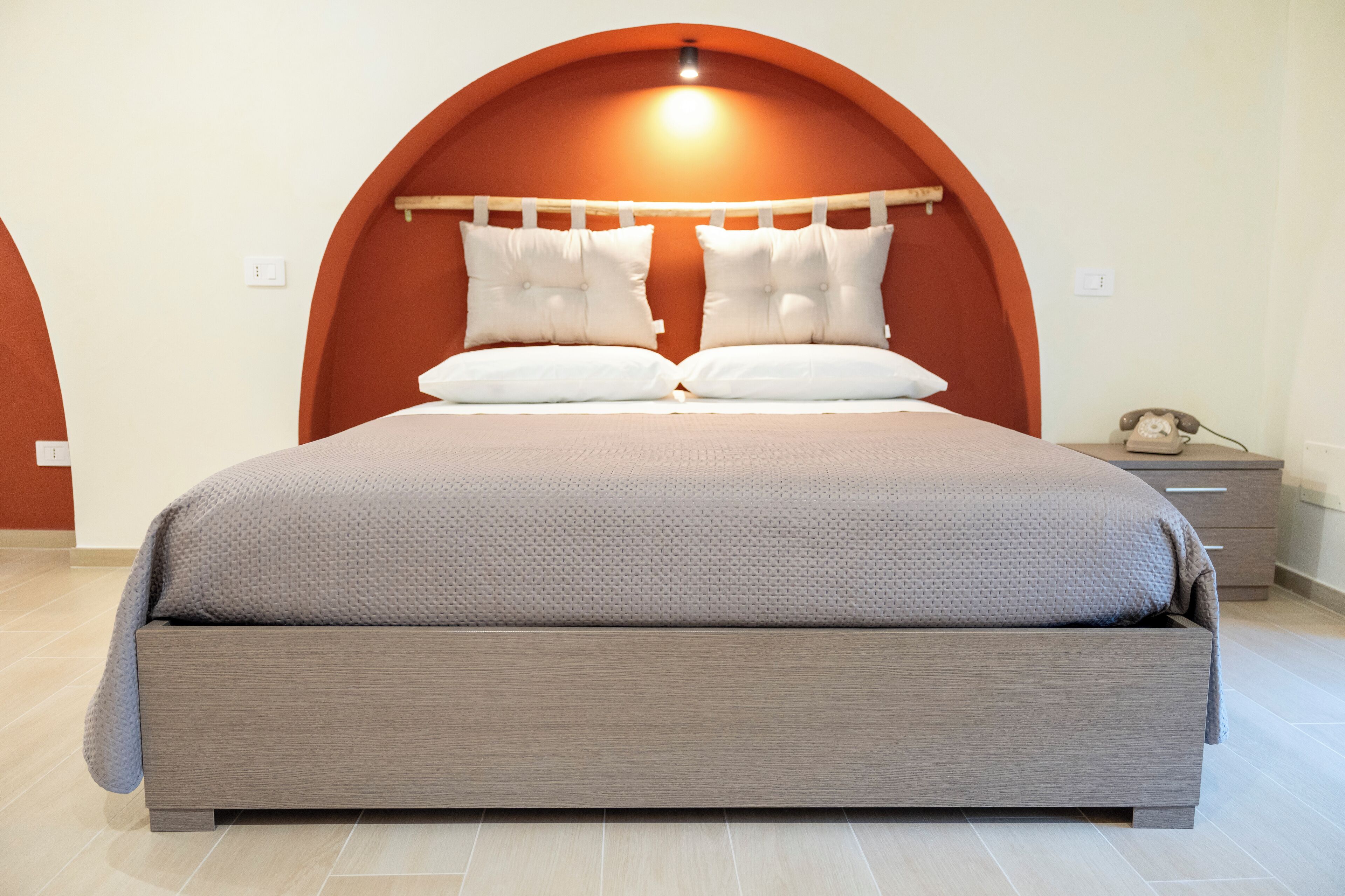 Ein modernes Schlafzimmer mit einem großen Bett, einem Holz-Kopfteil und einem Nachttisch mit Telefon.